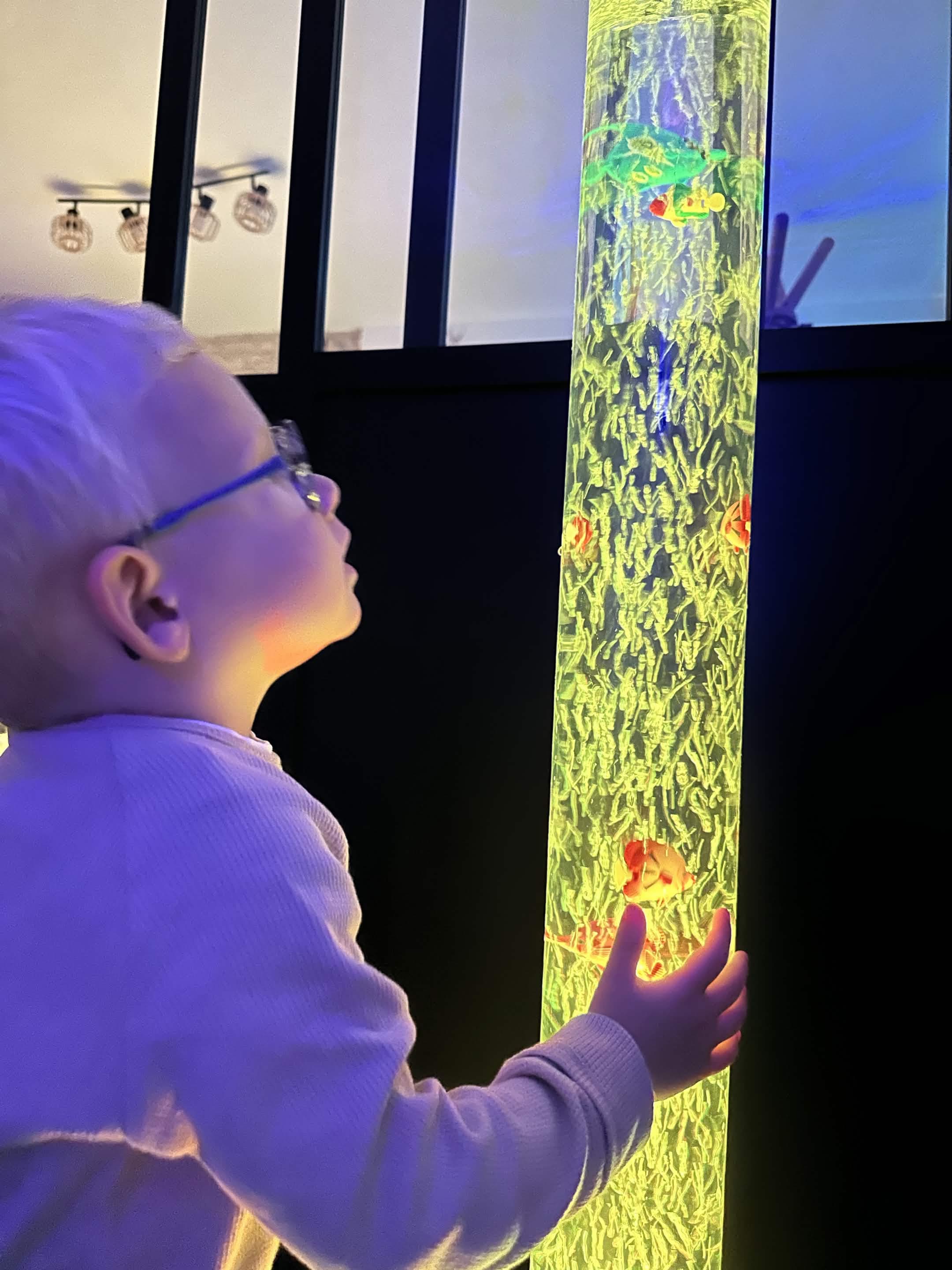 Enfant observe une colonne lumineuse pendant un atelier Snoezelen